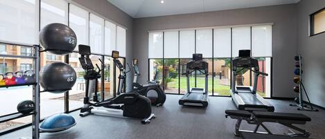 Un gimnasio con varios equipos de ejercicio, ventanas amplias y vista al exterior.