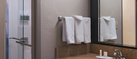 Un baño moderno con cabina de ducha de vidrio, lavamanos con encimera de granito y un espejo grande.