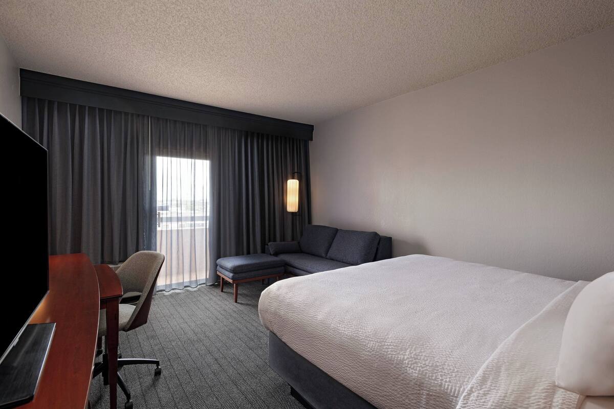 A hotel room with a large bed, a desk, a chair, and a sofa.