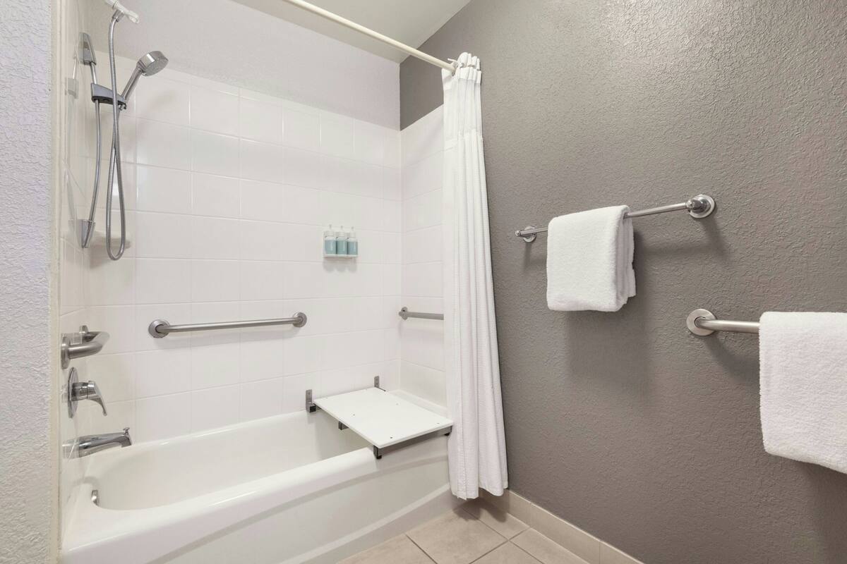 A bathroom with a bathtub, shower, grab bars, and a towel rack.