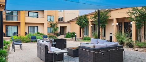 Un patio con mobiliario exterior, incluyendo sofás y sillones de mimbre, rodeado por un toldo azul.
