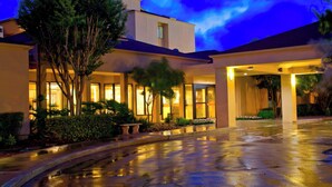 A hotel entrance with a wet driveway, large windows, and a tree in the foreground. - Courtyard by Marriott San Antonio Airport (San Antonio)