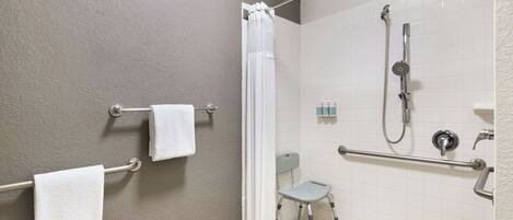 A bathroom with a shower, grab bars, a wheelchair-accessible bench, and a towel rack.