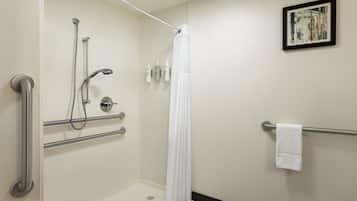 A bathroom with a shower, grab bars, a towel rack, and a framed picture on the wall.