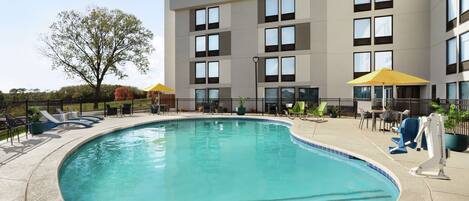 A swimming pool with lounge chairs and umbrellas, surrounded by a building with multiple windows and balconies.