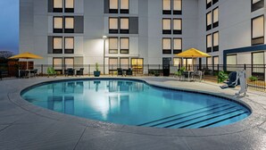 A modern building with a swimming pool, outdoor seating, and umbrellas. - Hampton Inn Kansas City-Airport (Kansas City)