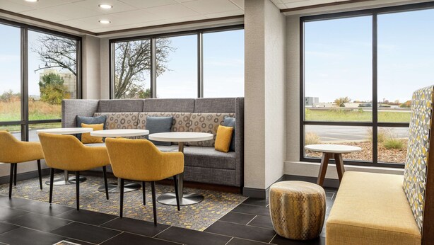 A modern indoor seating area with a sofa, yellow chairs, and a round table. - Hampton Inn Kansas City-Airport (Kansas City)