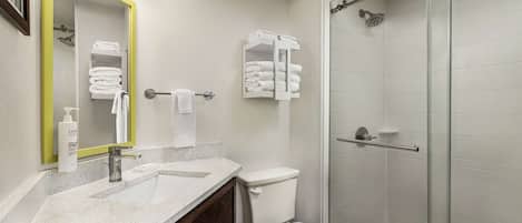 A bathroom with a white sink, mirror, and toilet. There is a glass shower enclosure and a towel rack with folded towels.
