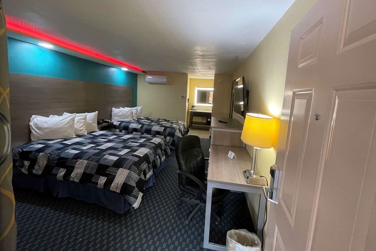 Ein Hotelzimmer mit zwei Betten, einem Schreibtisch, einem Stuhl, einem Fernseher und einer Lampe.