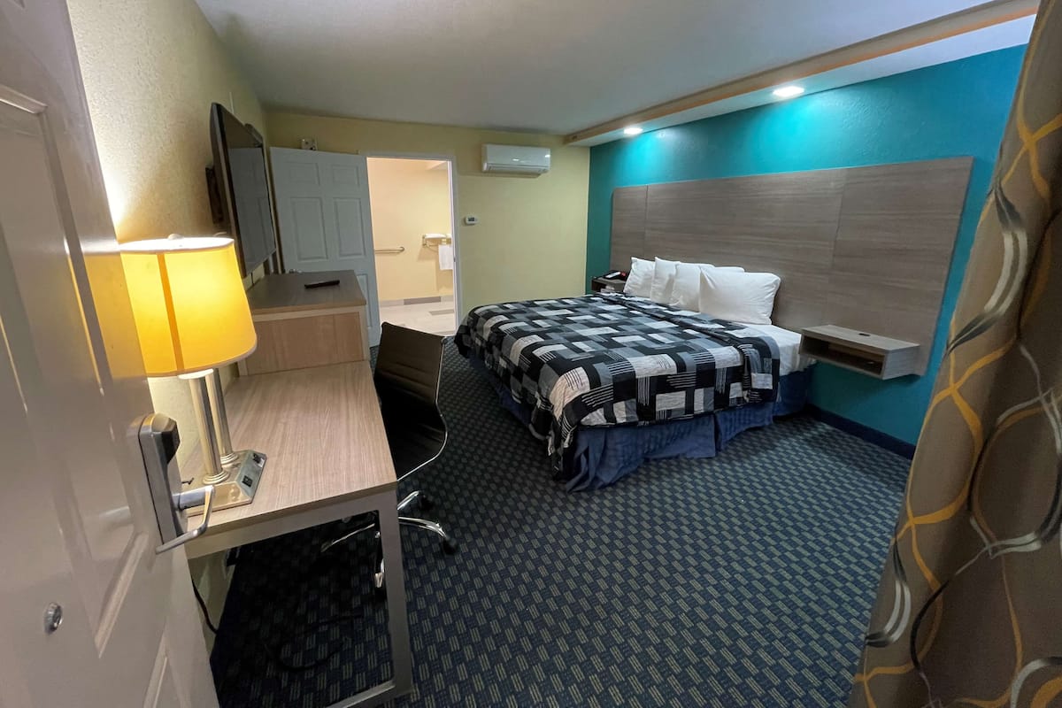 Ein Hotelzimmer mit einem Bett, einem Schreibtisch mit Lampe, einem Fernseher und einem durch eine offene Tür einsehbaren Badezimmer.
