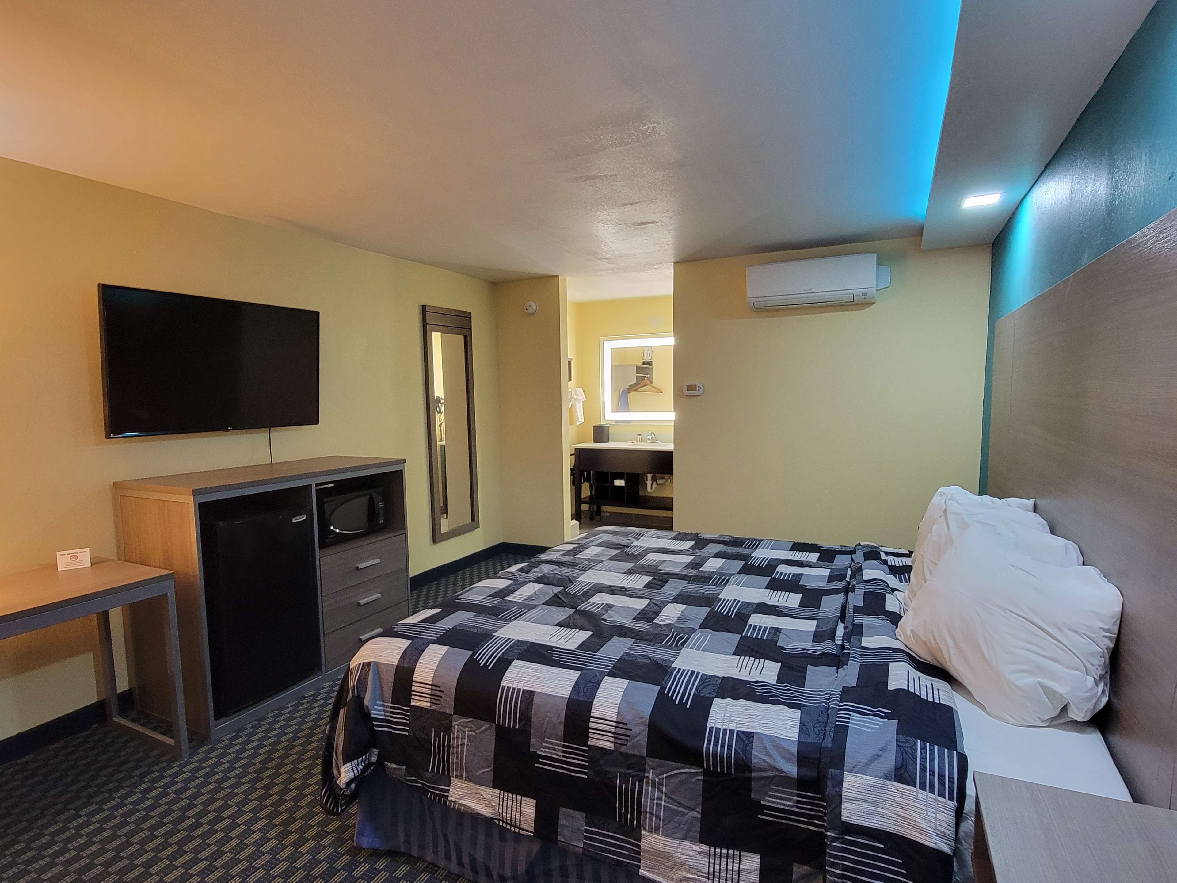 Una habitación de hotel con cama, escritorio, televisor, espejo y unidad de aire acondicionado.