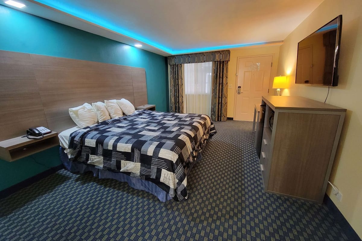 Ein Hotelzimmer mit einem Bett, einem Schreibtisch, einer Lampe, einem Fernseher und einer Tür.