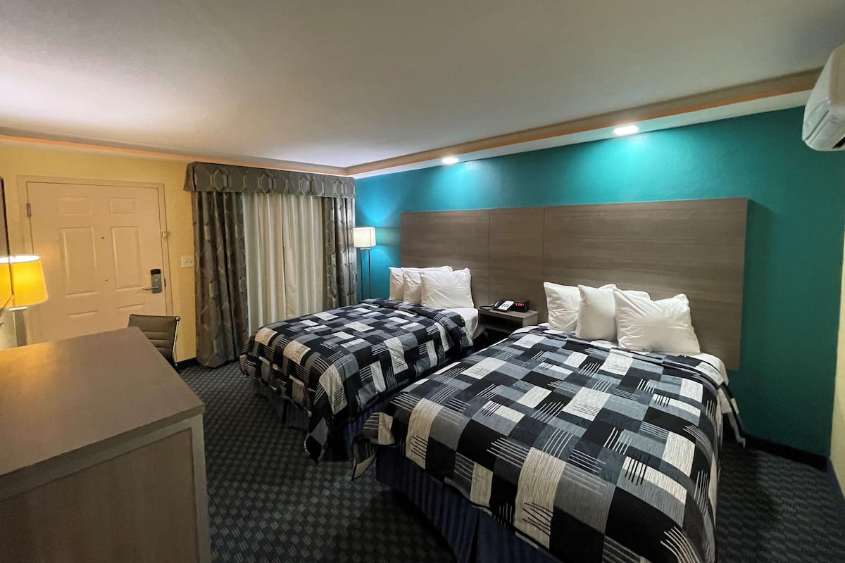 Ein Hotelzimmer mit zwei Betten, einem Schreibtisch, einem Stuhl, einer Lampe und einem Nachttisch mit Telefon.