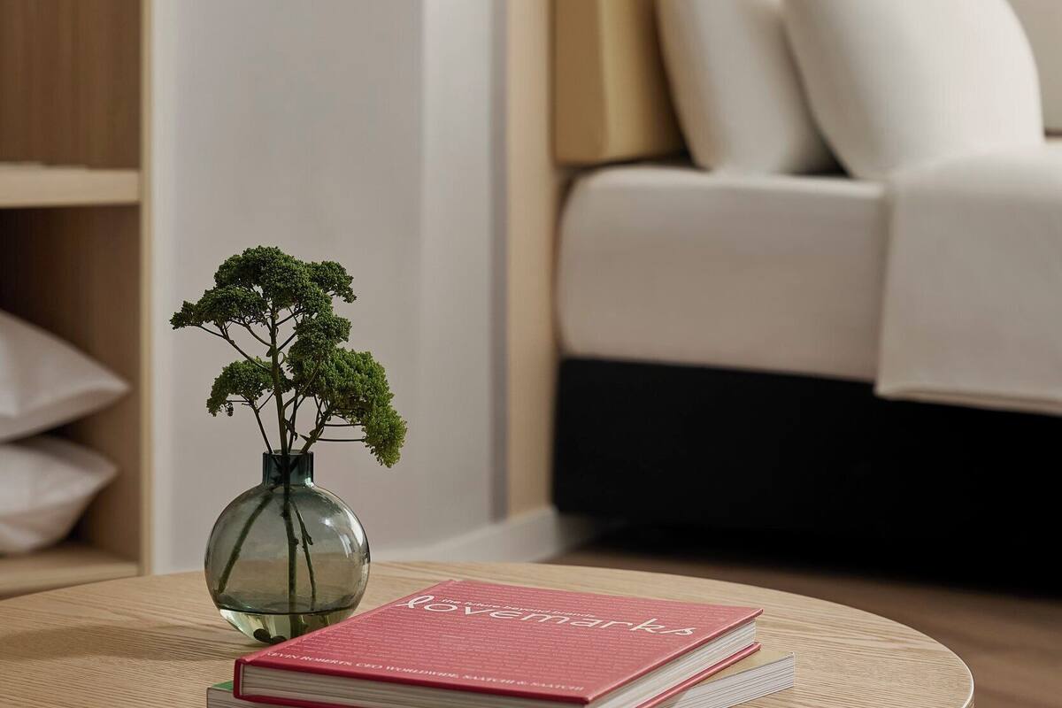 A round wooden table with a book and a glass vase with a plant.