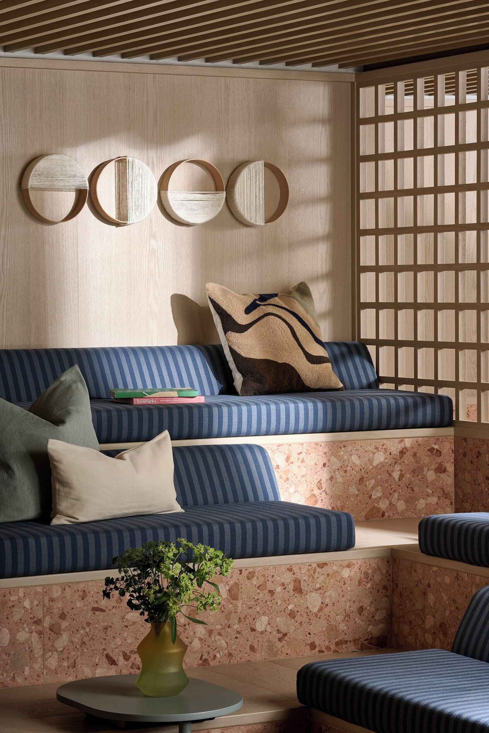 A modern living room with a blue-striped sofa, a round coffee table with a vase, and a wooden wall with circular decorations.
