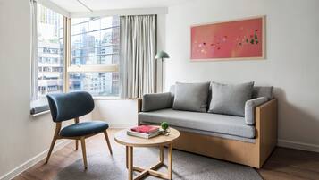 Un salon moderne avec un canapé, un fauteuil, une petite table ronde et une grande fenêtre avec des rideaux.