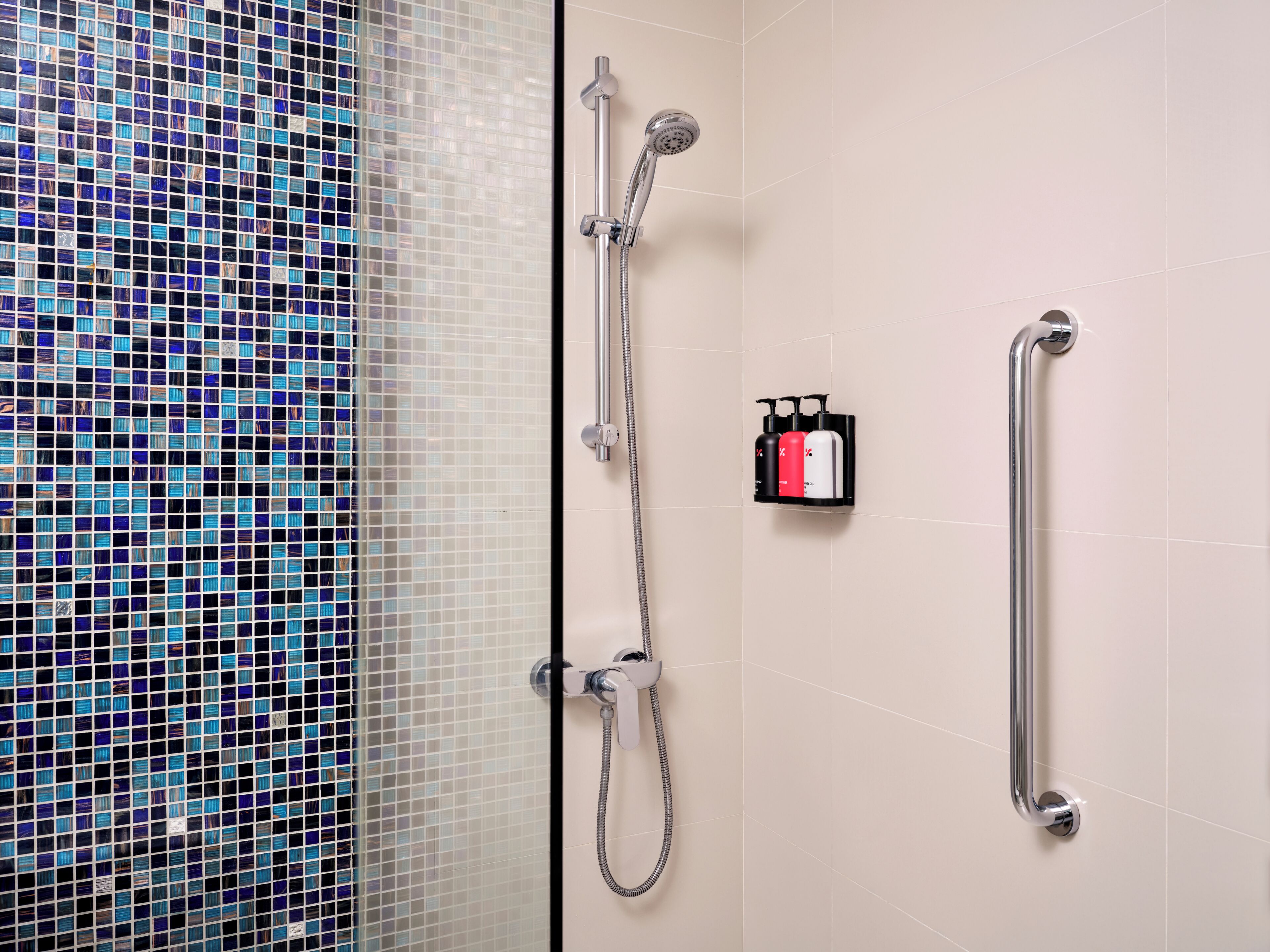 A shower with a handheld showerhead and a handheld shower attachment, a grab bar, and a soap dispenser on the wall.