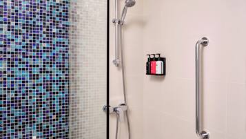 A shower with a handheld showerhead and a handheld shower attachment, a grab bar, and a soap dispenser on the wall.
