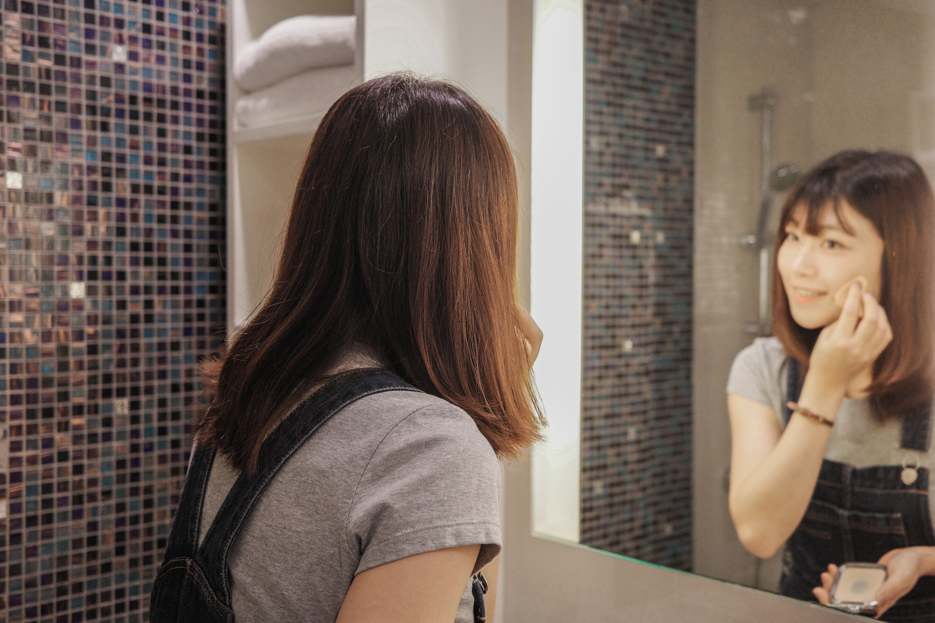 A person standing in front of a bathroom mirror with a tiled wall behind them.