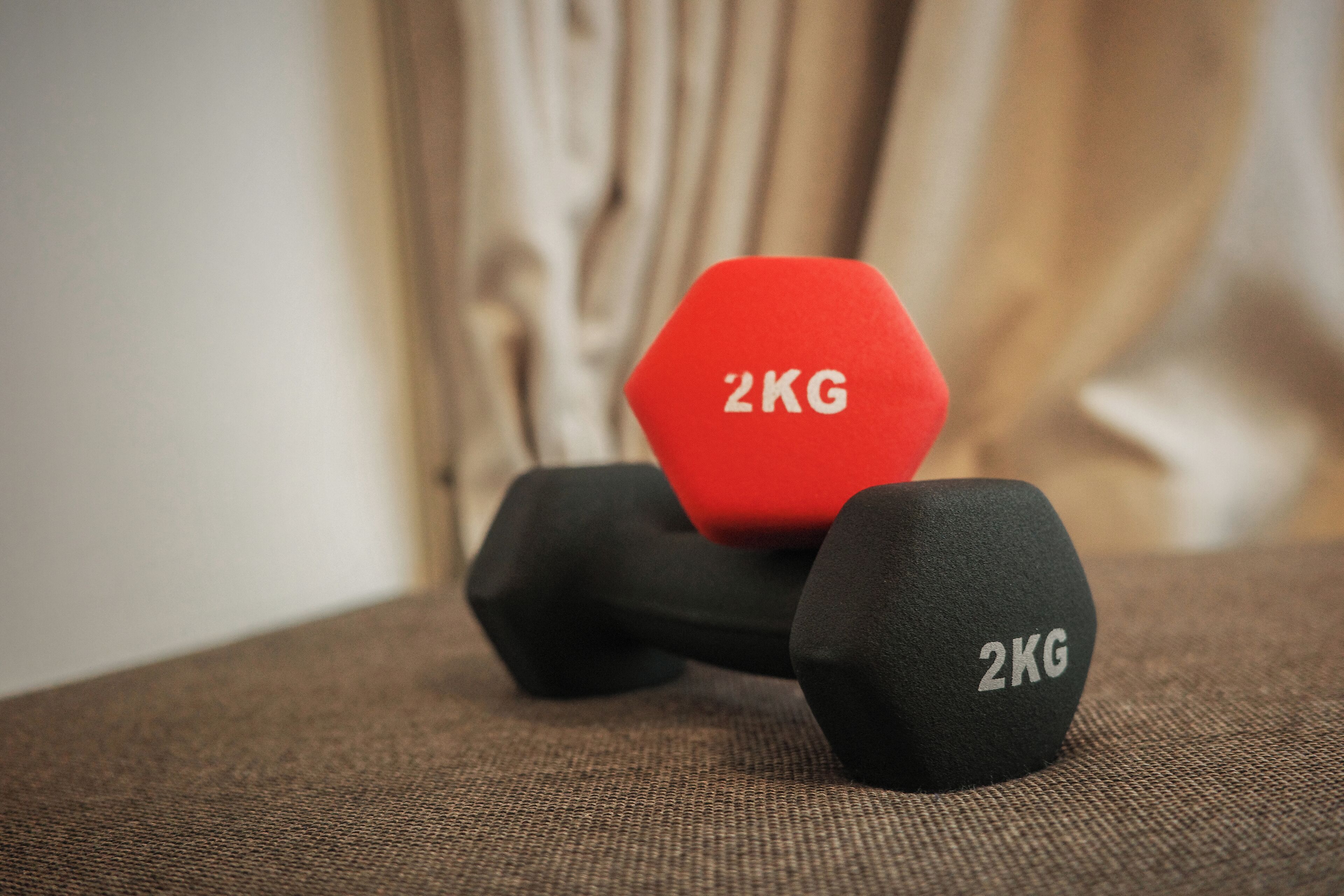 Two dumbbells, one red and one black, with "2KG" marked on them, placed on a textured surface.