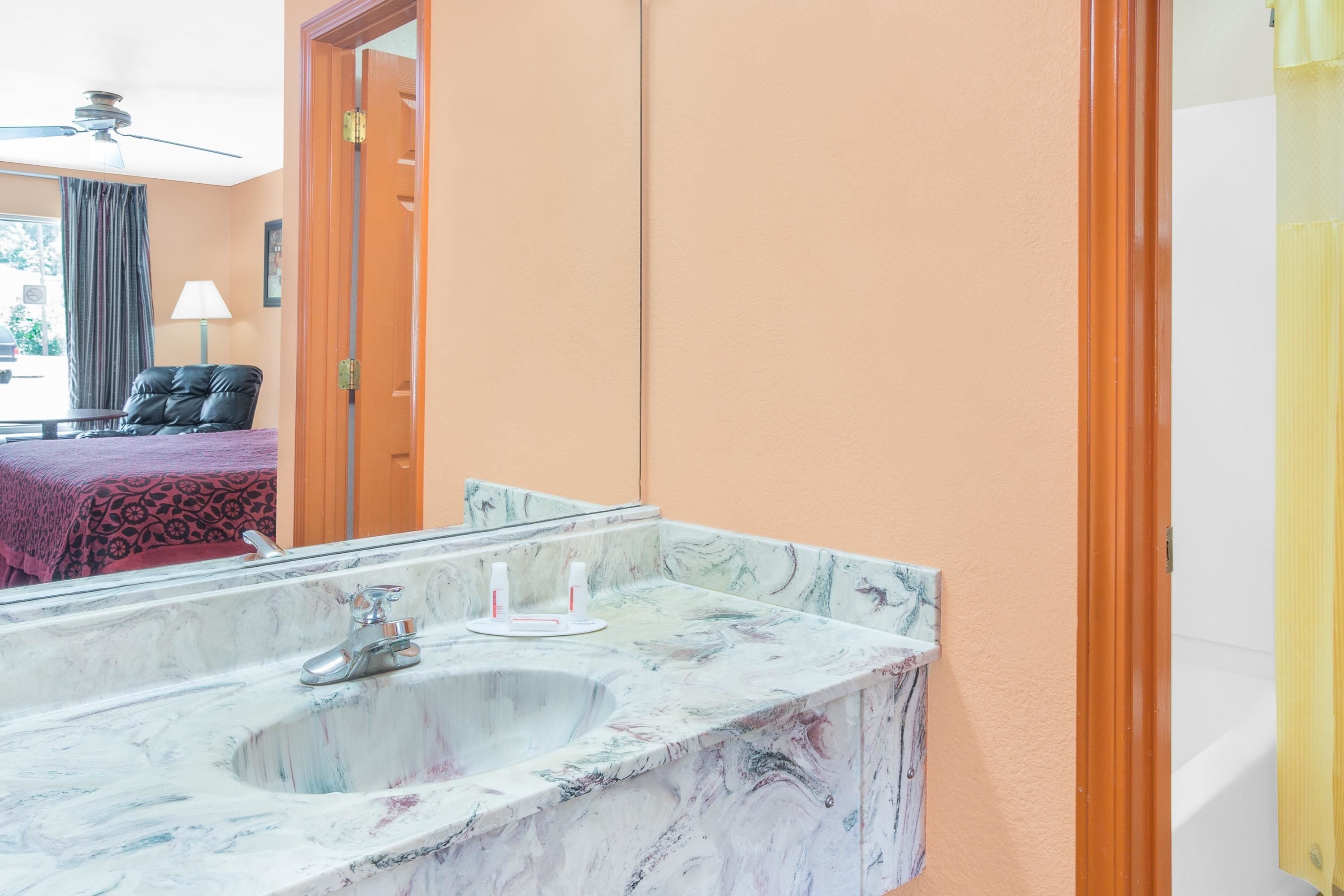 Un baño con lavamanos de mármol, un espejo y una puerta que da a otra habitación.