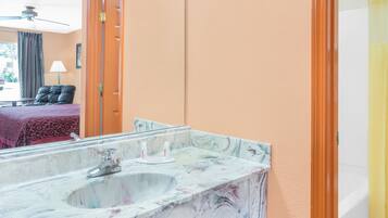 Une salle de bain avec un lavabo en marbre, un miroir et une porte donnant sur une autre pièce.