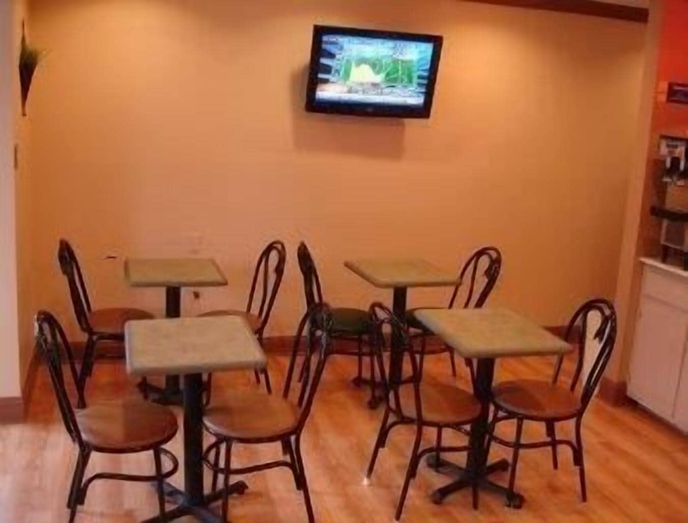 Una habitación con cuatro mesas y sillas, un televisor montado en la pared, y piso de madera.