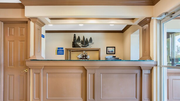 A reception area with a wooden door, a framed ship model, and a framed picture on the counter. - Americas Best Value Inn Kosciusko (Kosciusko)