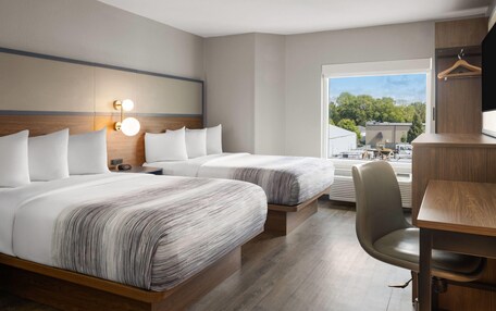 A modern hotel room with two beds, a desk, and a chair.