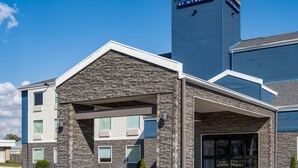 Un hotel con fachada de piedra, un acceso cubierto y un estacionamiento.