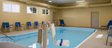 An indoor swimming pool with blue chairs, a pool lift, and a door in the background.