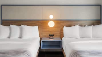 A hotel room with two beds, a nightstand with a clock, and a wall-mounted light fixture.