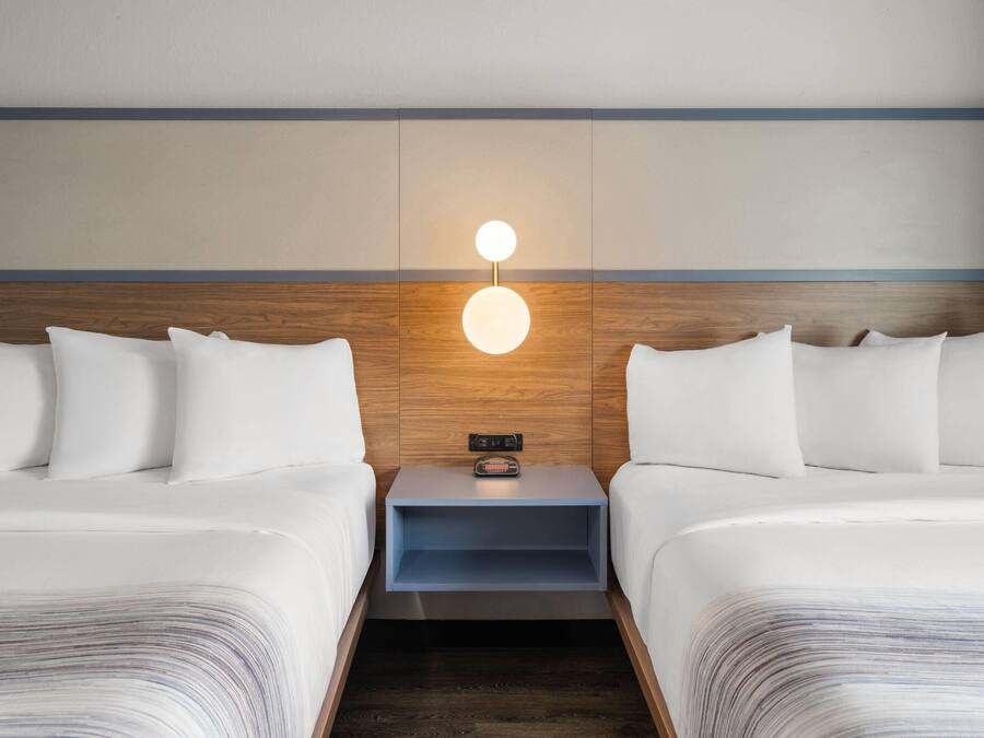 A hotel room with two beds, a nightstand with a clock, and a wall-mounted light fixture.