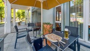 Eine Terrasse im Freien mit Tisch, Stühlen, einer Pizza, einem Bierkrug und einem Blumentopf.