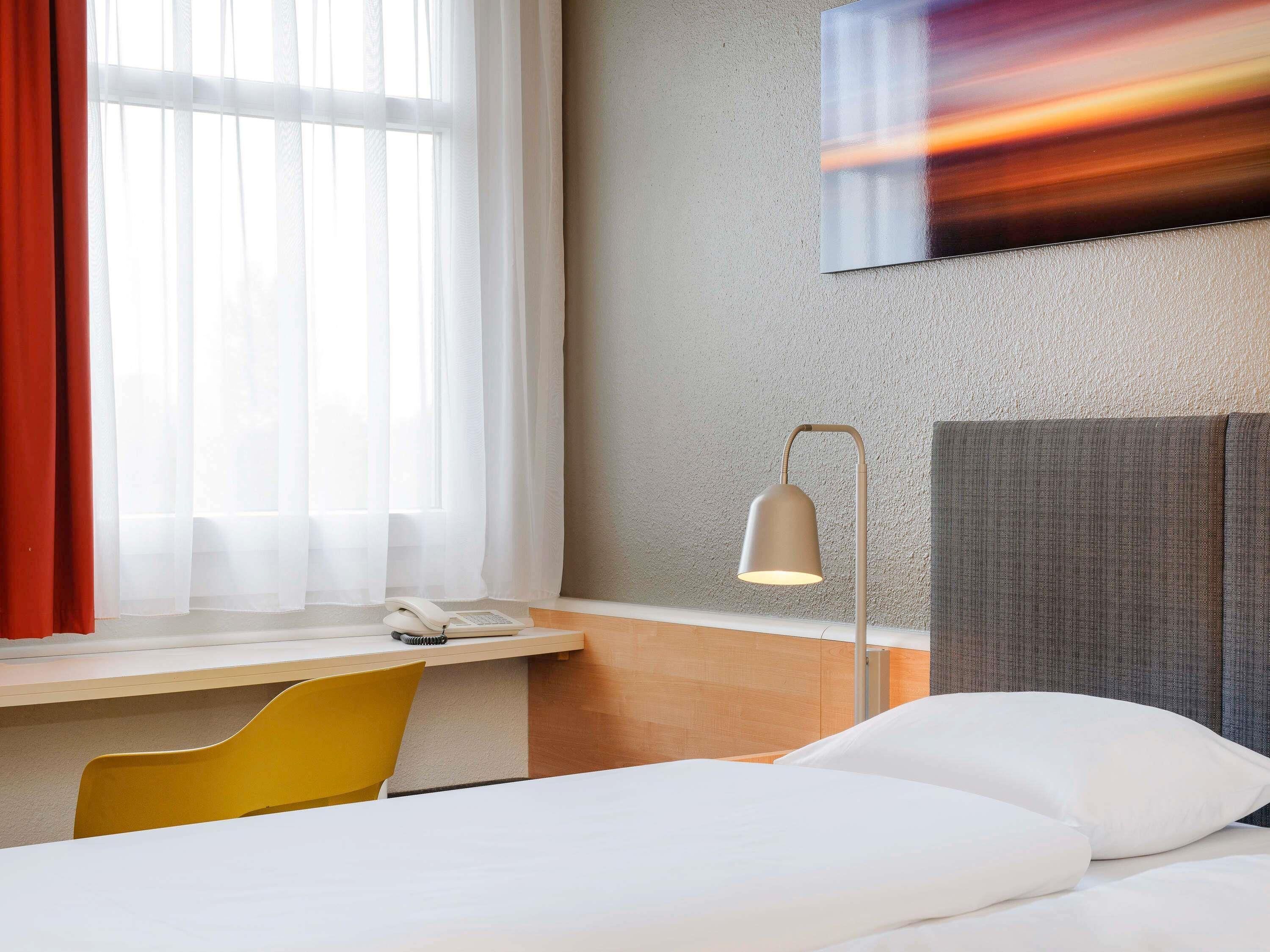 Ein Hotelzimmer mit einem Bett, einem Schreibtisch mit Telefon, einer Lampe und einem Sessel.