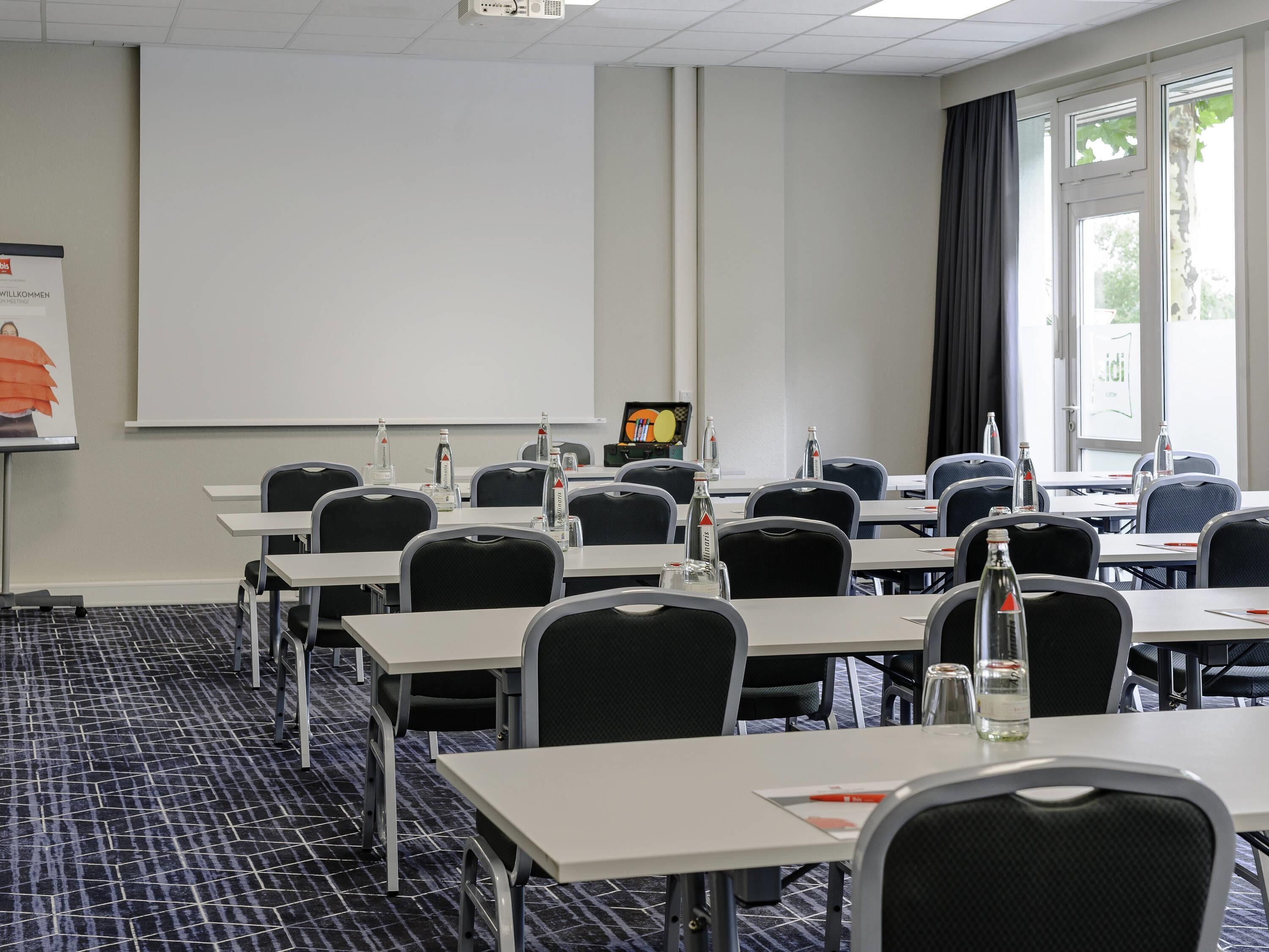 A conference room with tables, chairs, a projector screen, and a presentation screen.