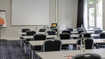 A conference room with tables, chairs, a projector screen, and a presentation screen.