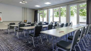 Una sala de conferencias con mesas, sillas, un proyector y grandes ventanales.
