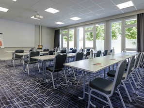 Una sala de conferencias con mesas, sillas, un proyector y grandes ventanales.