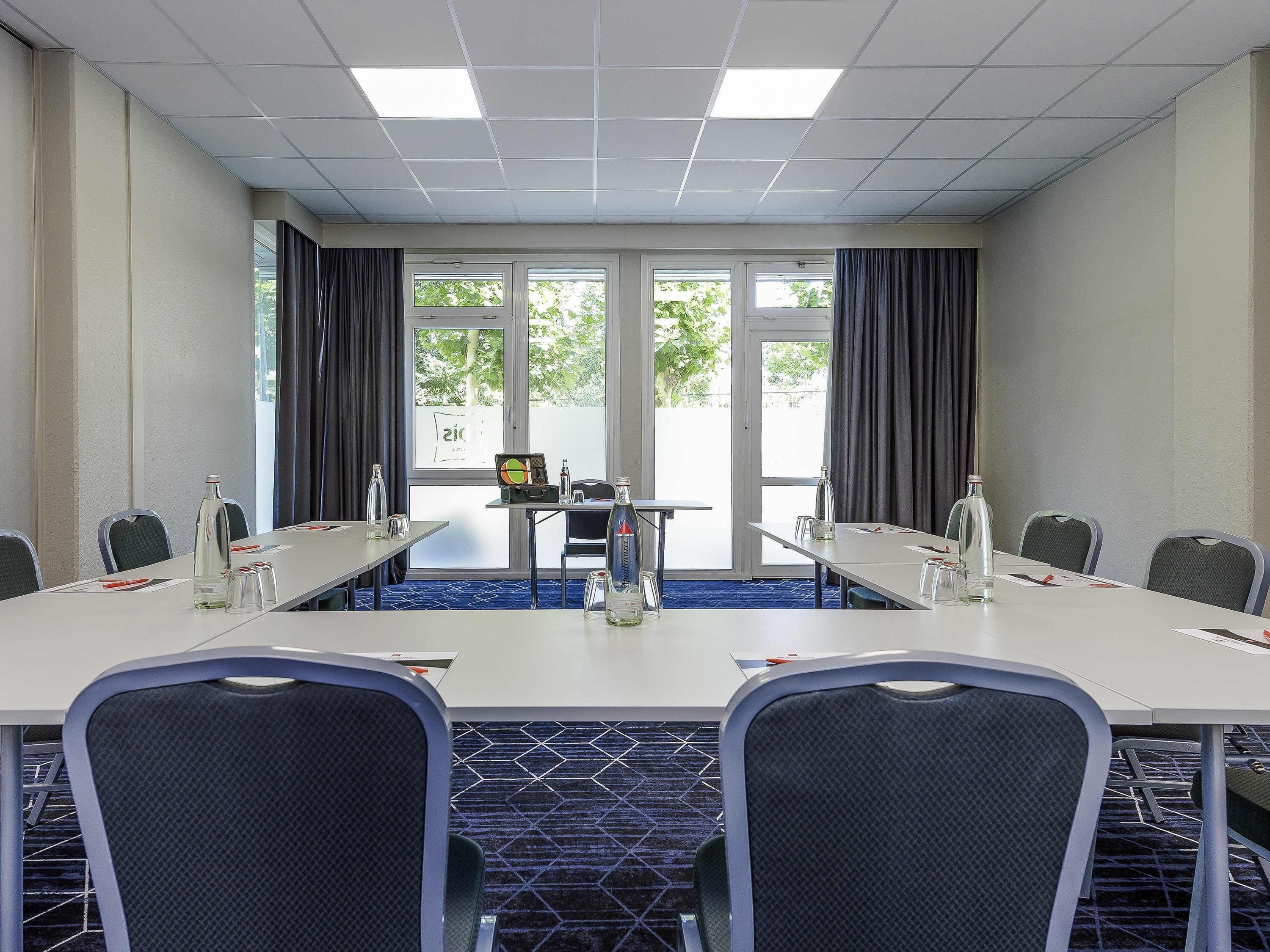 A conference room with a long table, chairs, a projector, and a window with curtains.