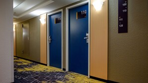 Ein Hotelgang mit nummerierten Türen, einem gemusterten Teppich und einem an der Wand befestigten Verzeichnis.
