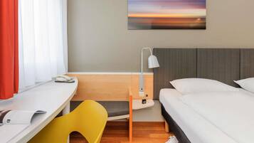 Ein Hotelzimmer mit Bett, Schreibtisch, Stuhl, Lampe und einem Gemälde an der Wand.