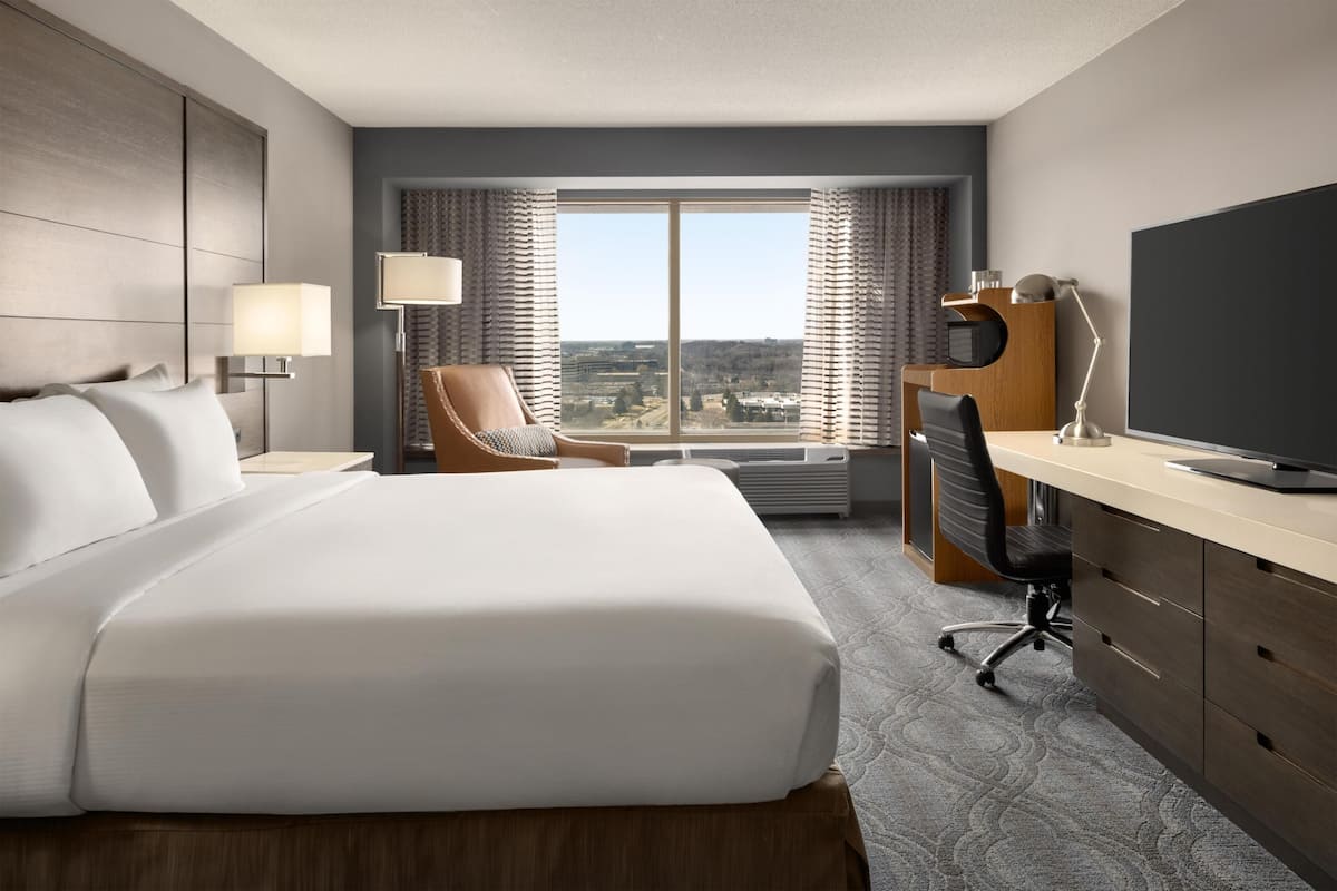Een hotelkamer met een groot bed, een bureau, een stoel, een televisie en uitzicht op de stad.