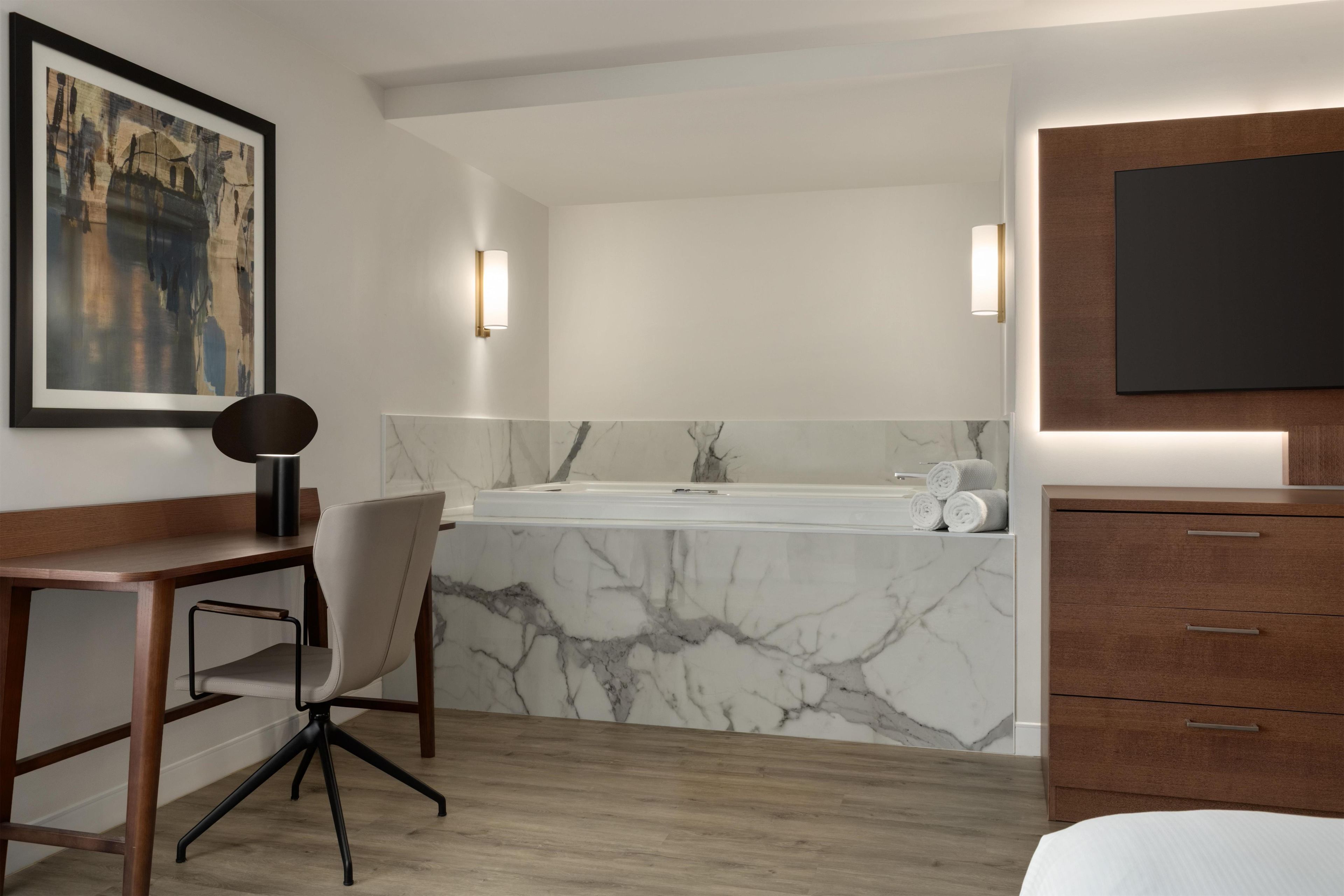 A modern bathroom with a marble sink, a bathtub, a wooden desk, and a chair.