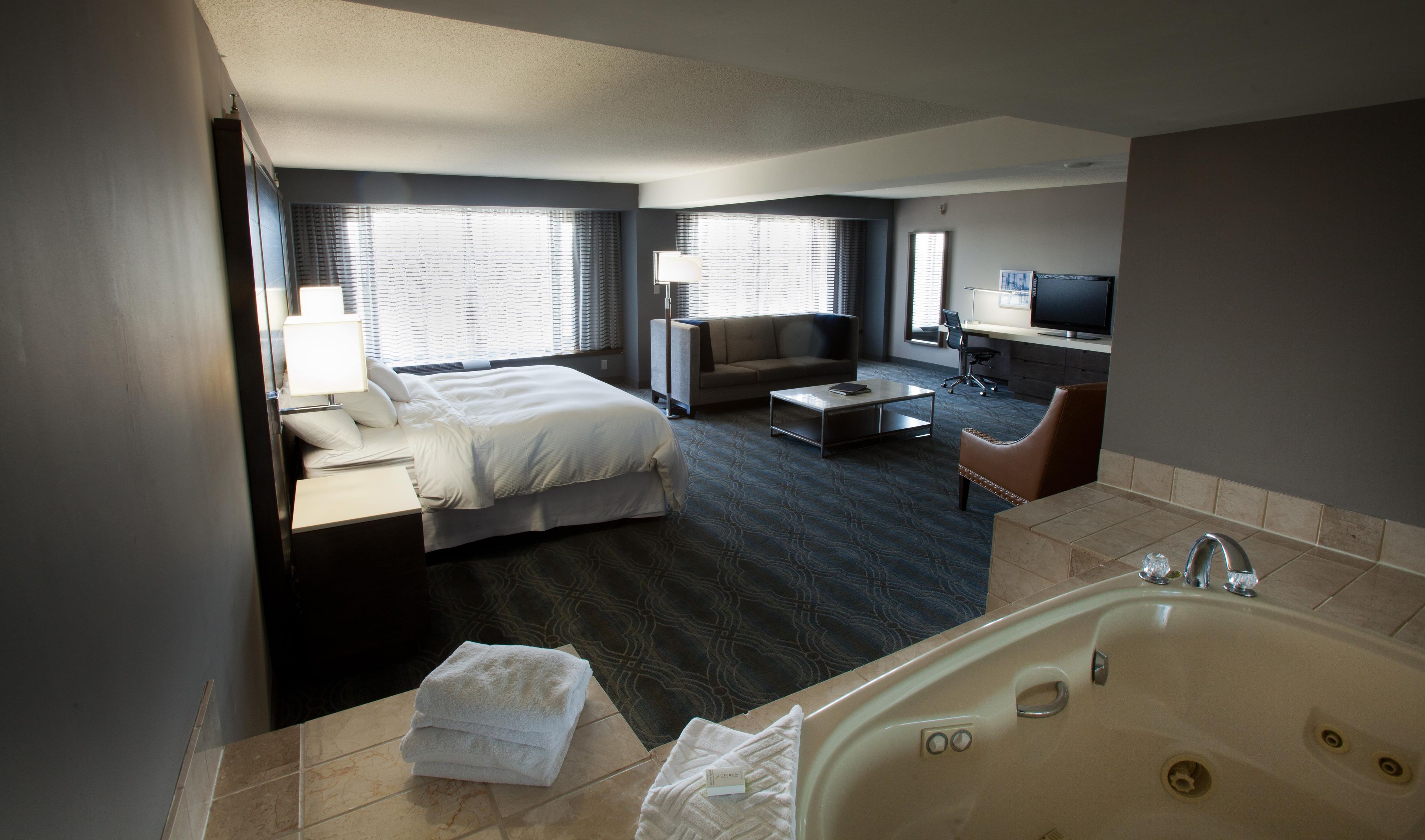 A hotel room with a bed, a sofa, a desk, a TV, and a bathroom with a bathtub.