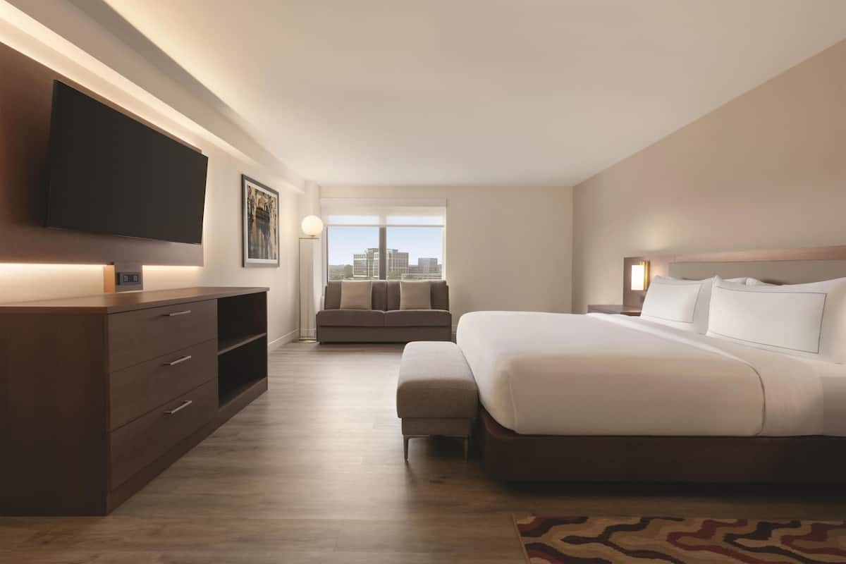 Hotelkamer met een groot bed, een aan de muur bevestigde televisie, een sofa en een raam met uitzicht over de stad.