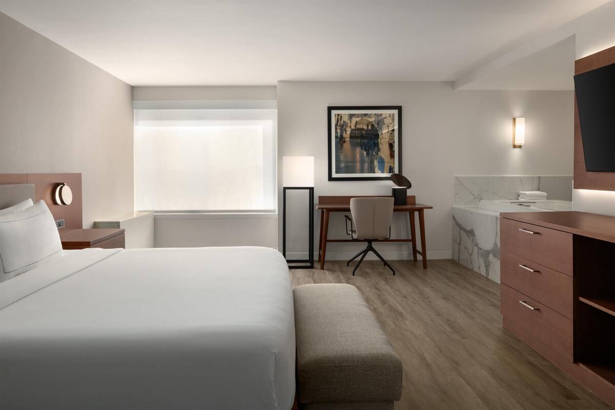 Hotelkamer met een bed, bureau, stoel, televisie, lamp en een badkamer met bad.