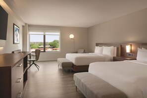A hotel room with two beds, a desk, a chair, a bedside table, a lamp, and a window with a view. - Doubletree by Hilton Bloomington - Minneapolis South (Bloomington)