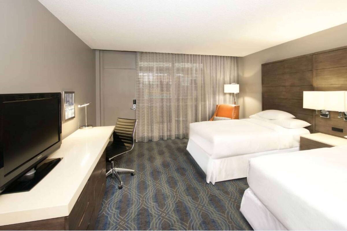 Een hotelkamer met een flatscreen televisie, twee bedden, een bureau en een kamerbreed tapijt met dessin.