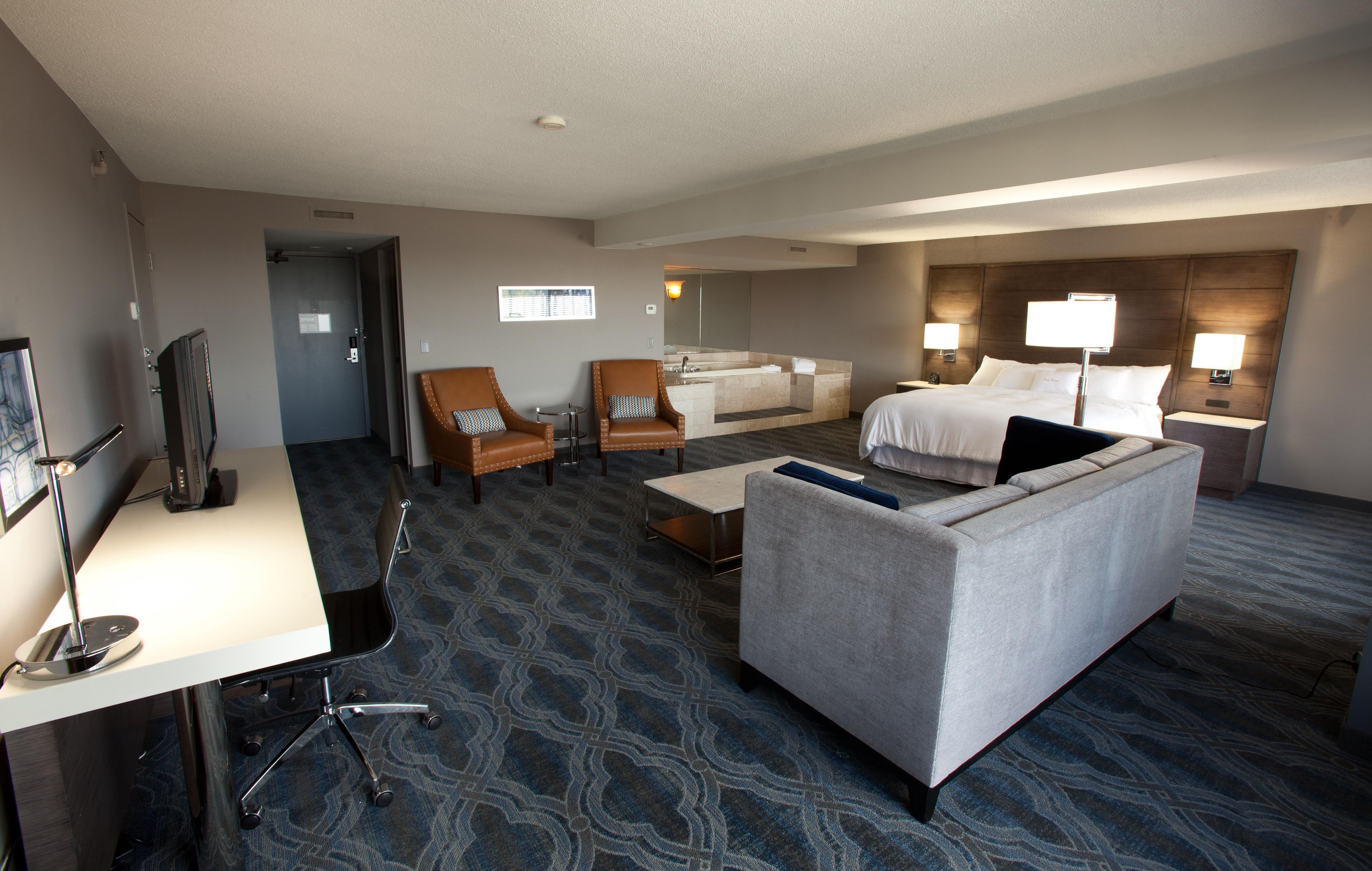 A hotel room with a bed, a sofa, a desk, a chair, a TV, and a bathroom.